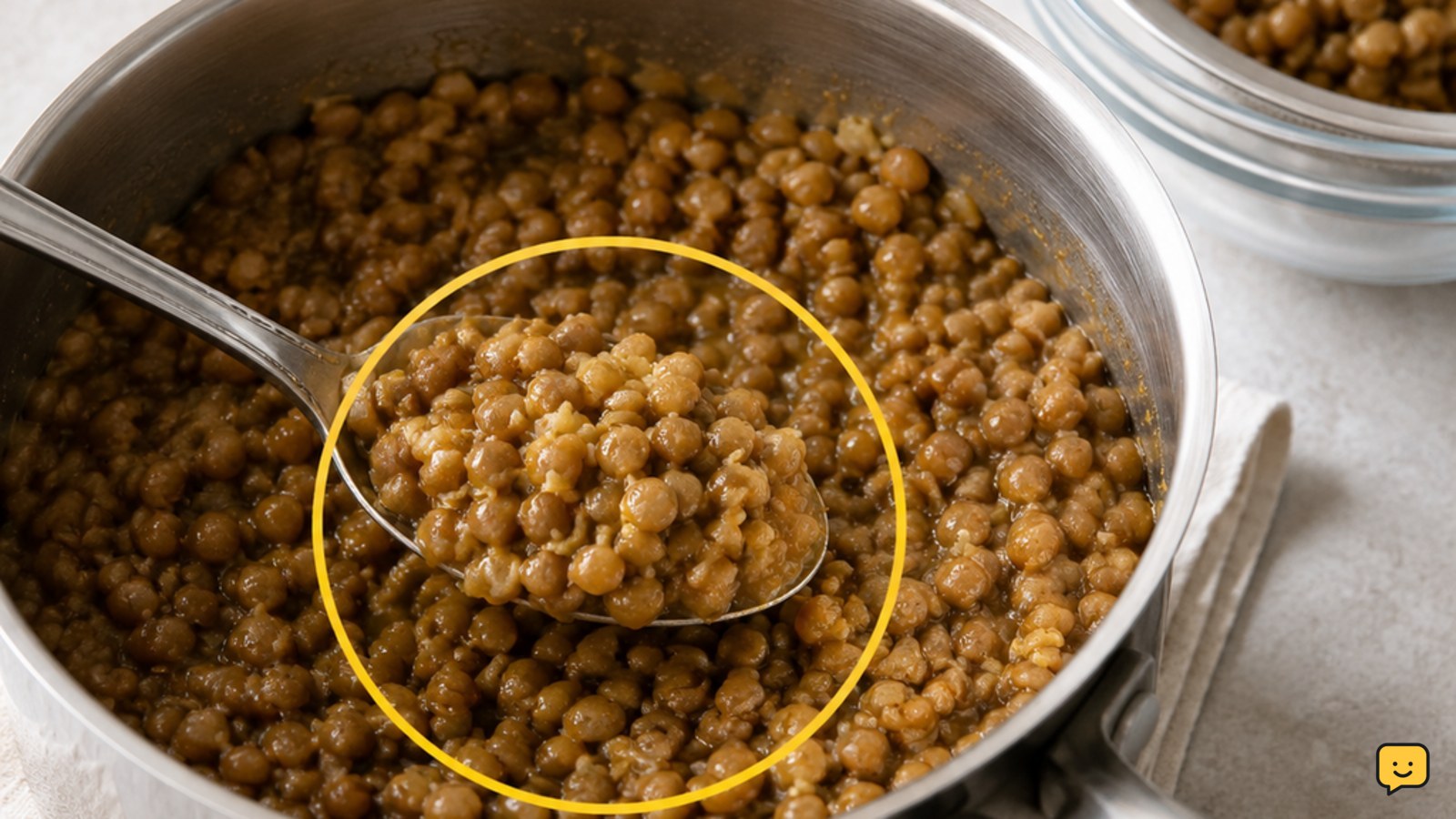 A saucepan of tender cooked lentils with a spoon and drained lentils nearby