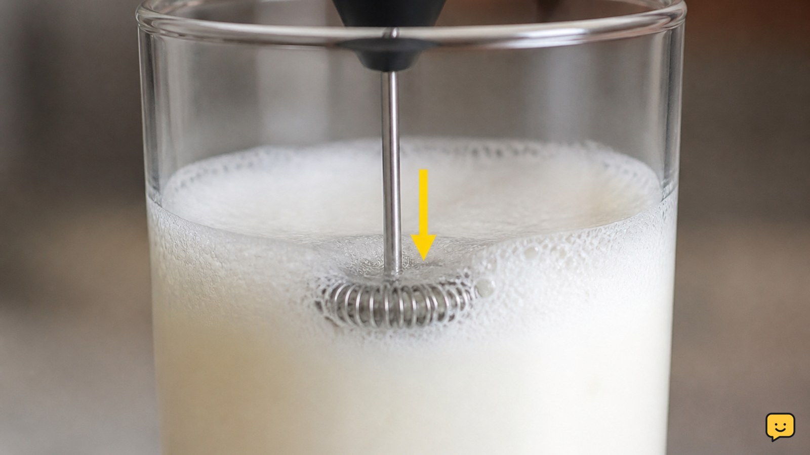 Handheld milk frother positioned just below the surface of cold milk in a narrow cup
